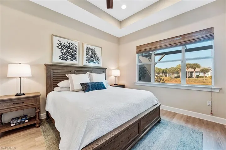 Bedroom with light wood-style flooring, a ceiling fan, and a tray ceiling