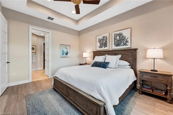 Bedroom featuring a raised ceiling, recessed lighting, a ceiling fan, light wood finished floors, and ensuite bathroom