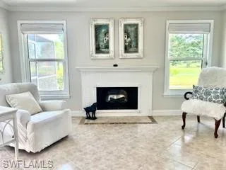 Living area with crown molding, a fireplace with flush hearth, and tile patterned floors