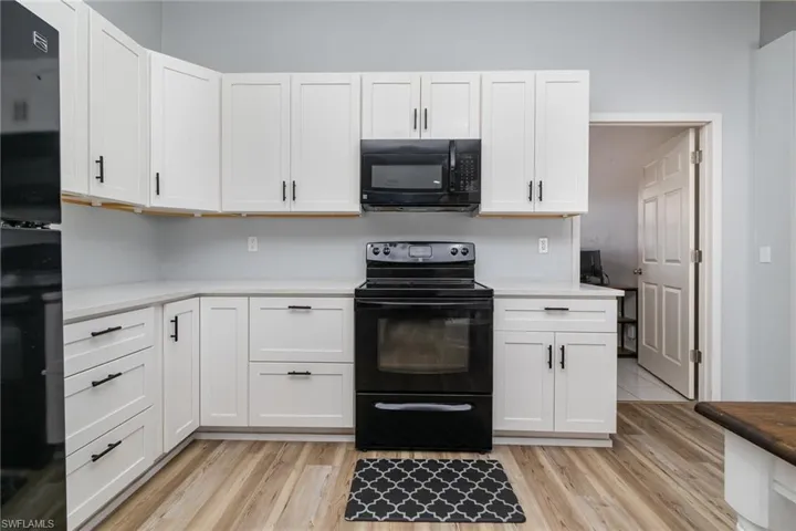 Kitchen featuring white cabinets, light hardwood / wood-style floors, and black appliances