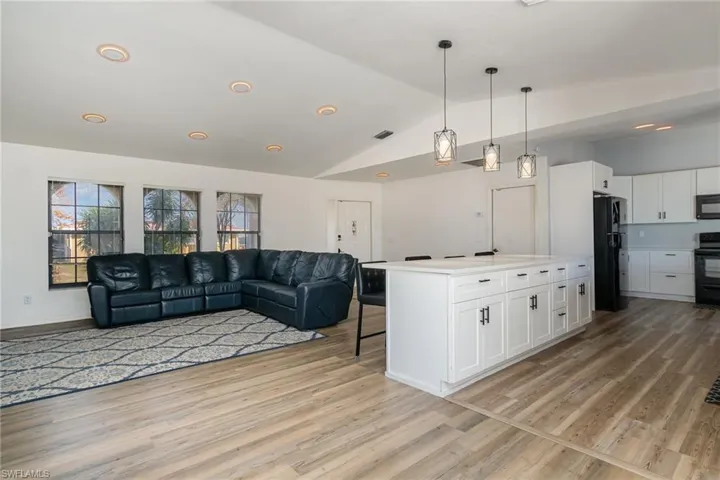 Kitchen with pendant lighting, white cabinetry, a center island, black appliances, and light hardwood / wood-style flooring