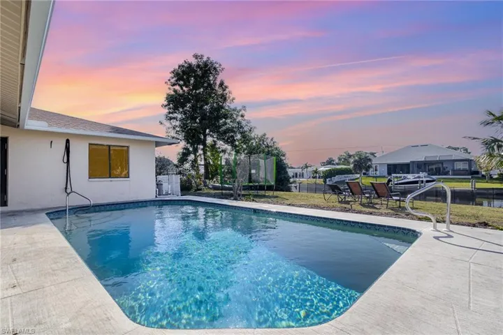 Pool at dusk with a patio area and a trampoline