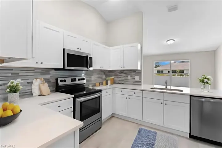 Kitchen with decorative backsplash, white cabinetry, appliances with stainless steel finishes, and sink