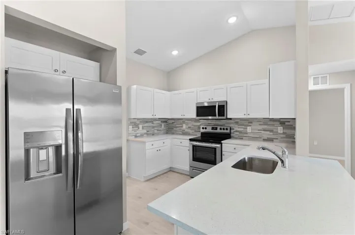 Kitchen with stainless steel appliances, sink, decorative backsplash, light wood-type flooring, and white cabinetry