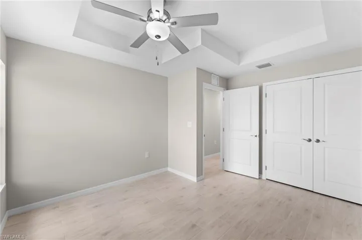 Unfurnished bedroom with a raised ceiling, light hardwood / wood-style flooring, a closet, and ceiling fan