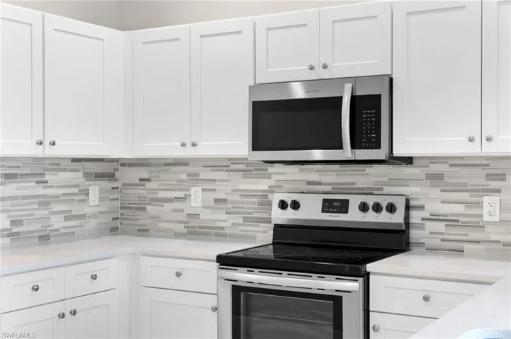Kitchen with white cabinetry, light stone counters, backsplash, and stainless steel appliances