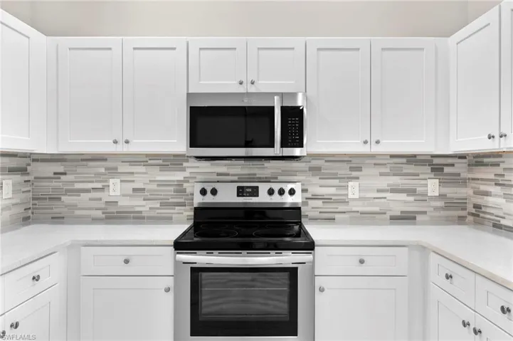 Kitchen featuring decorative backsplash, white cabinetry, light stone counters, and appliances with stainless steel finishes