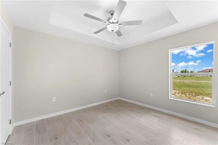 Spare room featuring ceiling fan, light hardwood / wood-style floors, and a tray ceiling