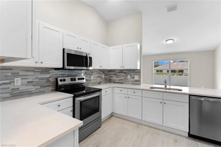 Kitchen with light hardwood / wood-style flooring, stainless steel appliances, backsplash, and white cabinets
