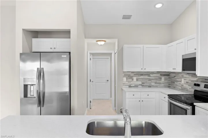 Kitchen featuring decorative backsplash, stainless steel appliances, light hardwood / wood-style flooring, and white cabinets