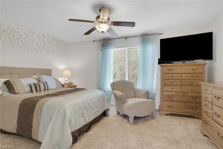 Bedroom with light carpet, ceiling fan, and a textured ceiling