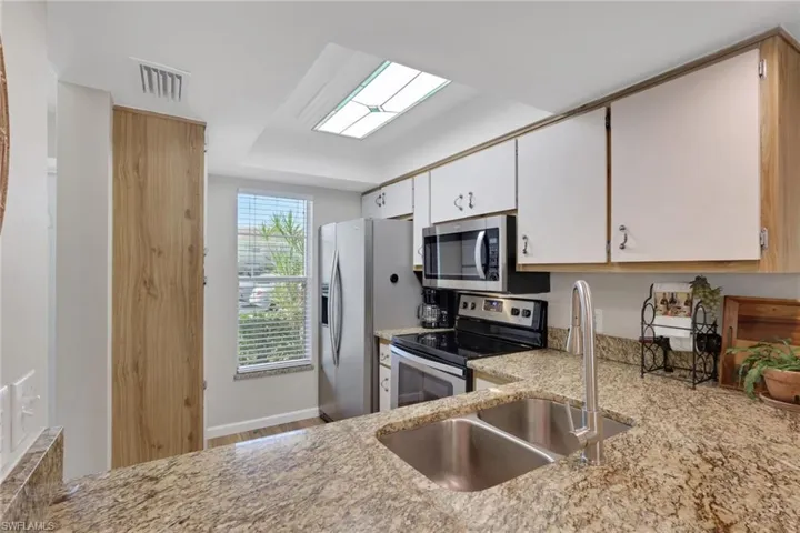 Kitchen featuring appliances with stainless steel finishes, white cabinets, light stone countertops, and light wood finished floors