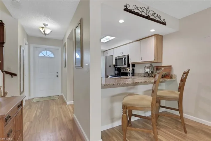 Kitchen with a textured ceiling, a kitchen breakfast bar, light wood-style flooring, appliances with stainless steel finishes, and light stone countertops