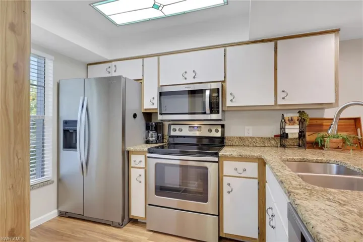 Kitchen with stainless steel appliances, white cabinetry, light wood-style flooring, and light stone counters