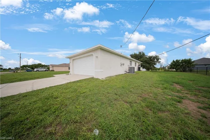 View of side of home featuring stucco siding, concrete driveway, a yard, and an attached garage
