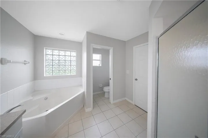Full bath with light tile patterned floors, a shower stall, a garden tub, and vanity