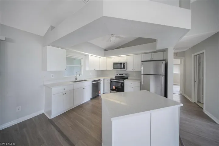 Kitchen featuring stainless steel appliances, white cabinetry, dark wood-type flooring, and light stone countertops