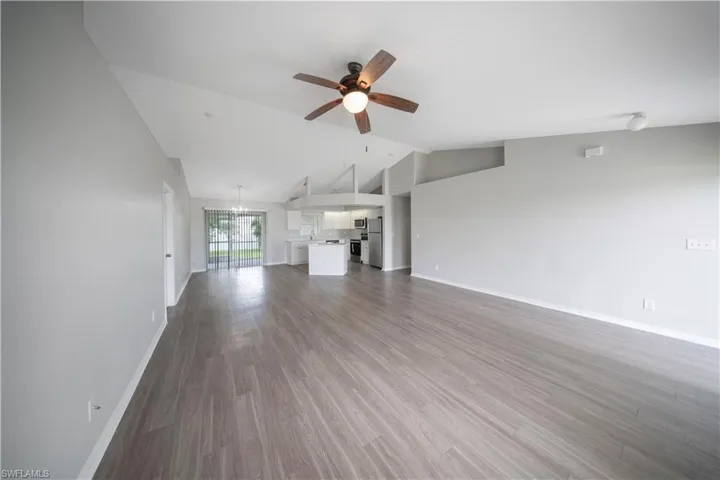 Unfurnished living room featuring lofted ceiling, dark wood finished floors, a ceiling fan, and a chandelier