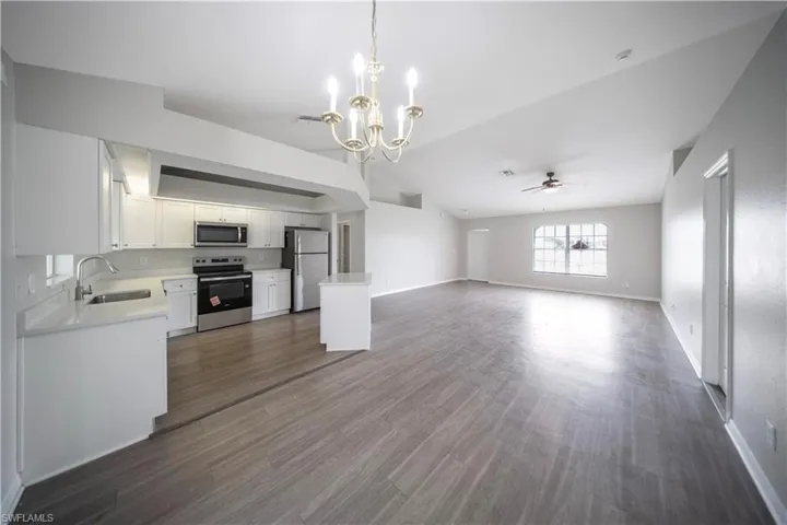 Kitchen featuring open floor plan, stainless steel appliances, white cabinets, lofted ceiling, and ceiling fan