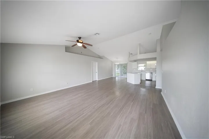 Unfurnished living room featuring dark wood-style flooring, ceiling fan, and vaulted ceiling