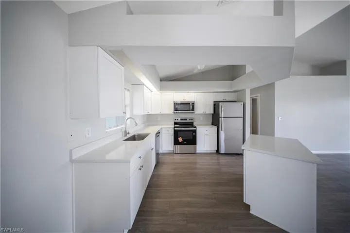 Kitchen featuring stainless steel appliances, white cabinetry, lofted ceiling, dark wood-style floors, and light stone countertops