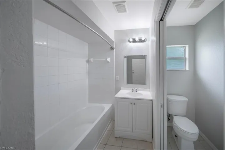 Bathroom featuring  shower combination, vanity, light tile patterned floors, and a textured wall