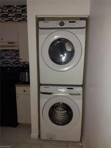 Laundry area with stacked washing maching and dryer and light tile flooring