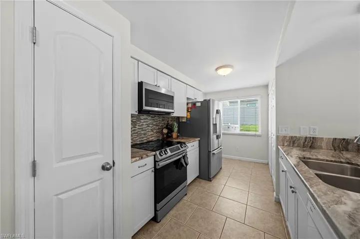 Kitchen featuring appliances with stainless steel finishes, decorative backsplash, light tile patterned floors, and white cabinetry