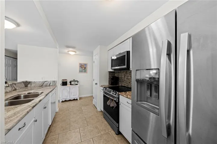 Kitchen featuring stainless steel appliances, backsplash, light tile patterned flooring, white cabinets, and light stone counters