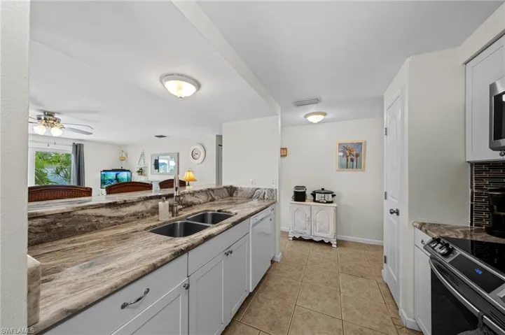 Kitchen featuring appliances with stainless steel finishes, light tile patterned flooring, a ceiling fan, white cabinets, and light stone countertops