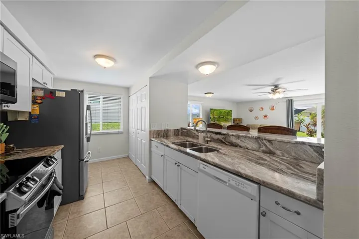 Kitchen featuring appliances with stainless steel finishes, light tile patterned flooring, a ceiling fan, stone countertops, and white cabinetry