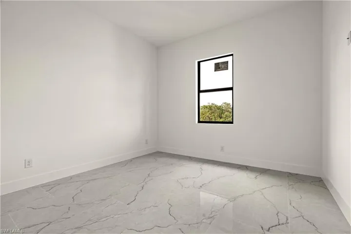 Unfurnished room featuring light marble finish flooring and baseboards