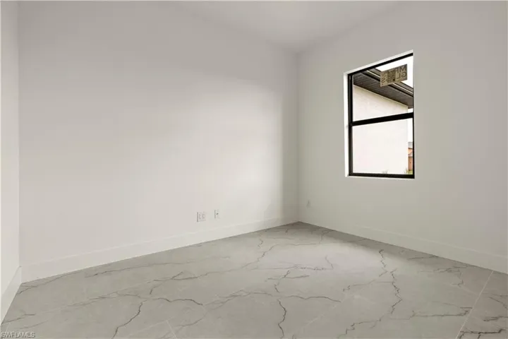 Unfurnished room featuring marble look tiles and baseboards