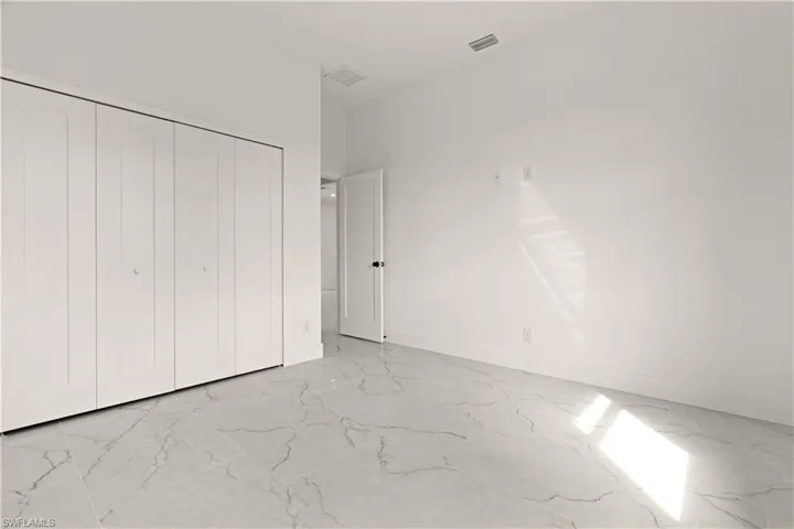 Unfurnished bedroom featuring light marble finish flooring, a closet, and baseboards
