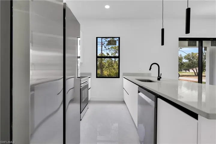 Kitchen with modern cabinets, a sink, baseboards, appliances with stainless steel finishes, and white cabinetry