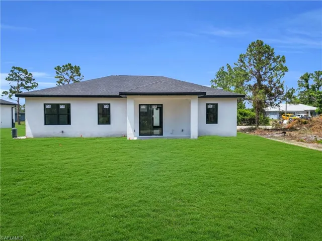 Back of house with stucco siding, a yard, and roof with shingles