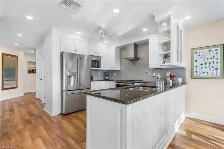 The Kitchen boasts a wall chimney range hood, granite countertops with glass tile backsplash, appliances with stainless steel finishes, and ample cabinetry.