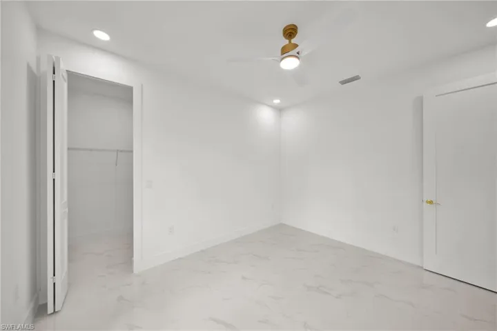 Unfurnished bedroom featuring light marble finish flooring, recessed lighting, a spacious closet, and a ceiling fan
