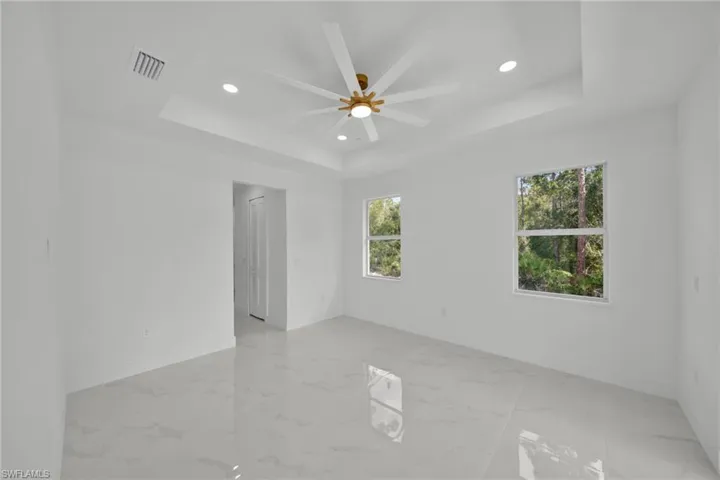 Unfurnished room with a raised ceiling, recessed lighting, ceiling fan, and light marble finish flooring
