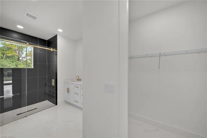 Bathroom with marble tiled floors, a stall shower, vanity, recessed lighting, and a walk in closet