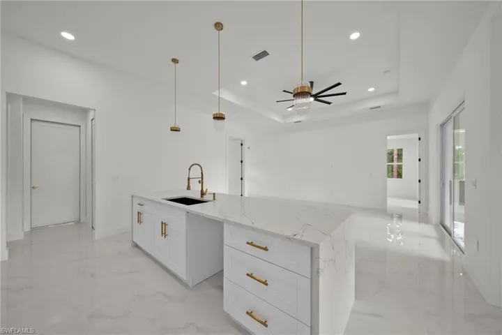 Kitchen featuring light marble finish flooring, a center island with sink, a raised ceiling, recessed lighting, and white cabinetry