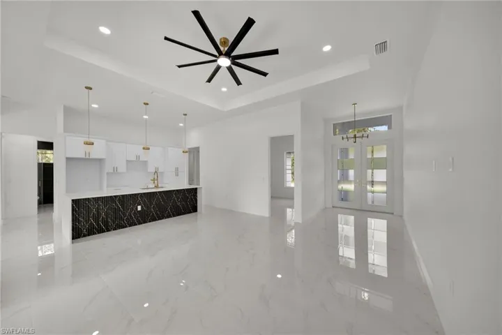 Unfurnished living room featuring a tray ceiling, recessed lighting, french doors, light marble finish flooring, and a chandelier