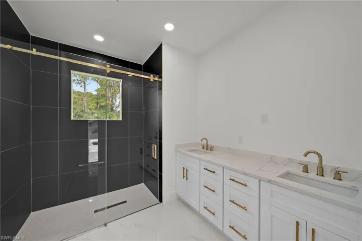 Full bathroom featuring a shower stall, double vanity, marble finish floors, and recessed lighting