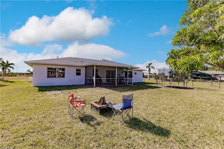 Back of property featuring a trampoline, an outdoor fire pit, and a lawn