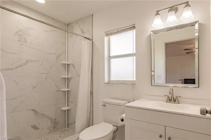 Bathroom featuring a shower with curtain, vanity, toilet, and ceiling fan