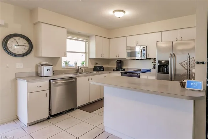 Kitchen with white cabinetry, sink, light tile patterned floors, and stainless steel appliances