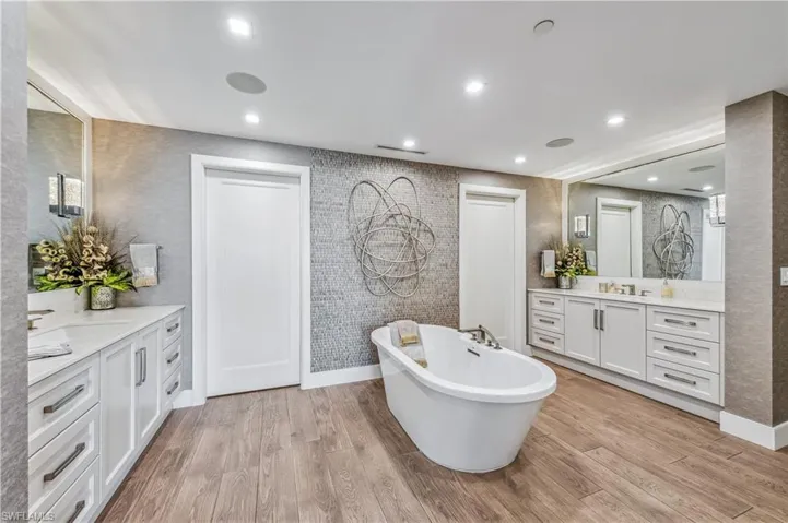 Master Full Bathroom with a free standing bath tub, two vanities, walk in closet through two doors, and recessed lighting