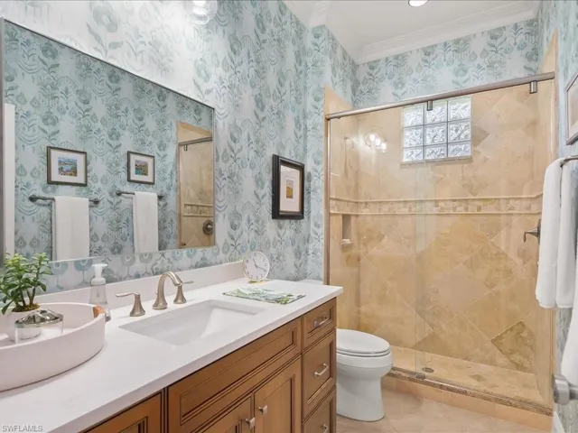 Full bathroom featuring a stall shower, vanity, crown molding, and wallpapered walls