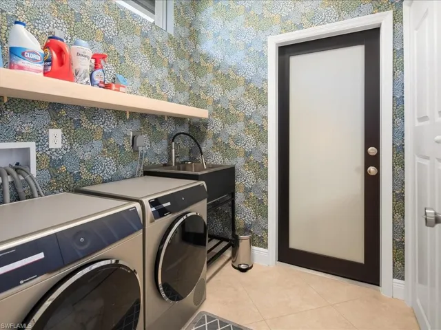 Laundry room with light tile patterned floors, wallpapered walls, and washing machine and dryer