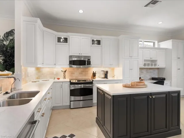 Kitchen with stainless steel appliances, glass insert cabinets, ornamental molding, backsplash, and two tone cabinetry